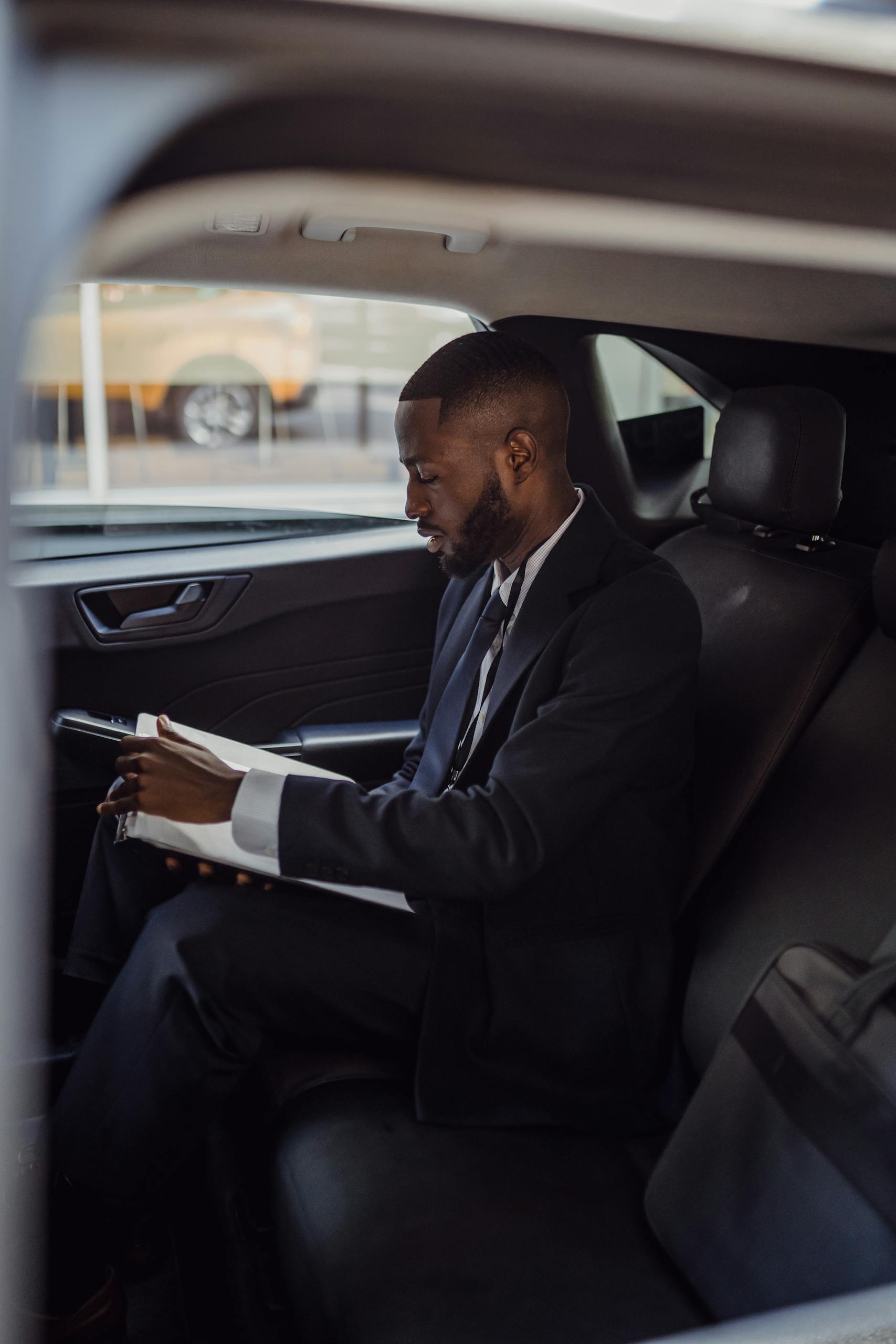 A business professional in a suit reading documents inside a car.